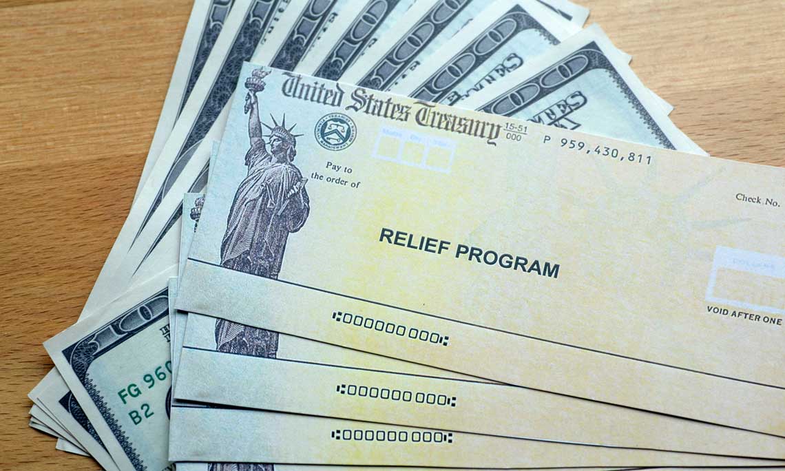 Sample relief program checks in front of hundred dollar bills