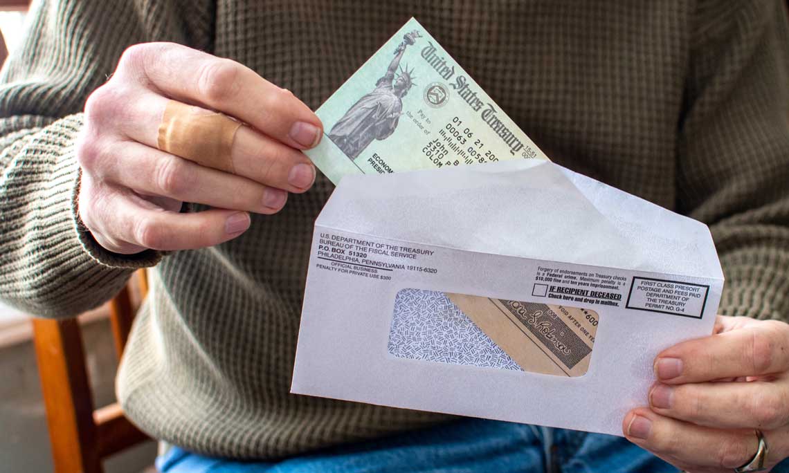 Man in green shirt holding a covid relief check in an envelope