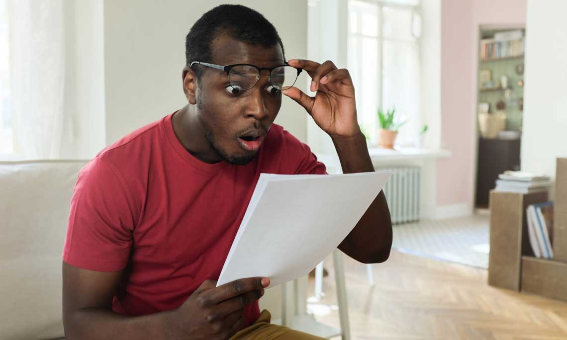 Surprised man looking at expensive utility bill while sitting down